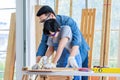 Asian professional male carpenter woodworker engineer dad in jeans outfit with safety gloves goggles helping teaching young boy Royalty Free Stock Photo