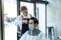 Asian professional male hairstylist combing and use scissors cutting young man customer`s hair in salon. Hairdresser wearing Royalty Free Stock Photo