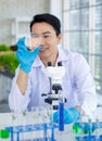 Asian professional male scientist researcher in white lab coat and rubber gloves sitting using microscope inspecting quality of Royalty Free Stock Photo
