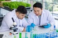 Asian professional male scientist researcher in white lab coat and rubber gloves sitting using microscope inspecting quality of Royalty Free Stock Photo