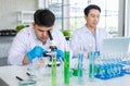 Asian professional male scientist researcher in white lab coat and rubber gloves sitting using microscope inspecting quality of Royalty Free Stock Photo