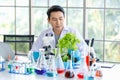 Asian professional male scientist researcher in white lab coat rubber gloves sitting using microscope looking at green salad Royalty Free Stock Photo