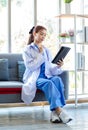 Asian professional successful female doctor in white lab coat with stethoscope sitting smiling holding tablet computer posing in Royalty Free Stock Photo