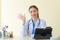 Asian professional successful female doctor in white lab coat with stethoscope sitting smiling at hospital office desk working