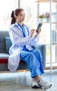 Asian professional successful female doctor in white lab coat with stethoscope sitting smiling using mobile phone posing in Royalty Free Stock Photo