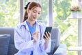 Asian professional successful female doctor in white lab coat with stethoscope sitting smiling using mobile phone posing in Royalty Free Stock Photo