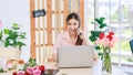 Asian professional successful female florist designer flower shop owner entrepreneur sitting on call via smartphone with customer