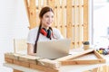 Asian professional thoughtful female carpenter worker staff with earphones in apron sitting holding pencil thinking ideas via