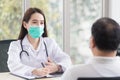 Asian professional  woman doctor wears medical coat and face mask while examines and talks with a man patient in hospital Royalty Free Stock Photo