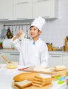 Asian professional young little boy pastry chef in white cooking uniform and tall cook hat standing using heart shape mold cutting Royalty Free Stock Photo