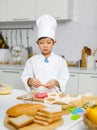 Asian professional young little boy pastry chef in white cooking uniform and tall cook hat standing using heart shape mold cutting Royalty Free Stock Photo