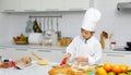 Asian professional young little boy pastry chef in white cooking uniform and tall cook hat standing using heart shape mold cutting Royalty Free Stock Photo