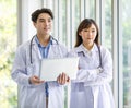 Asian professional young male and female intern doctor in white lab coat with stethoscope standing crossed arms holding laptop Royalty Free Stock Photo