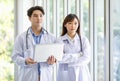 Asian professional young male and female intern doctor in white lab coat with stethoscope standing crossed arms holding laptop Royalty Free Stock Photo