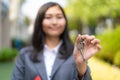 Asian real estate agent or realtor woman smiling and holding red file with showing house key in front of thier house in summer day Royalty Free Stock Photo