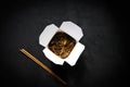 Asian restaurant food delivery. Soba noodles with meat, vegetables and soy sauce in white take-out paper box on black background Royalty Free Stock Photo