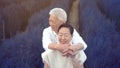 Asian retired senior couple hugging celebrating love in magical blue flower field togetehr happy