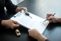 Asian salesman holding rental contract and hand over car key to client while he is holding pen to signing Royalty Free Stock Photo