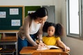 Asian school teacher assisting female student in classroom. Young woman working in school helping girl with her writing Royalty Free Stock Photo