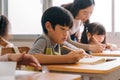 Asian school teacher assisting students in classroom. Young woman working in school helping boy with his writing Royalty Free Stock Photo