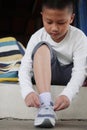 Asian schoolboy in casual clothing tying shoelaces on sneakers getting ready for school or traveling