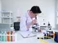 Asian scientist man looking and examining virus or bacteria by microscope equipment and note research result on paper for analysis Royalty Free Stock Photo