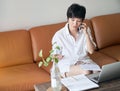 Asian self employed woman sitting on couch & working on laptop at home Royalty Free Stock Photo