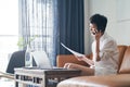 Asian self employed woman sitting on couch & working on laptop at home Royalty Free Stock Photo