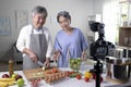 Asian senior couple blogger vlogger and online influencer recording video content on healthy food in the kitchen Royalty Free Stock Photo