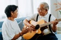 Asian senior couple sitting on the sofa and playing acoustic guitar together. Happy smiling elderly woman clapping hands Royalty Free Stock Photo