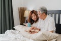 Asian senior couple talking on bed at home. Asian Senior Chinese grandparents, husband and wife happy drink coffee and read book