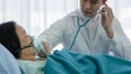 Asian senior female patient with oxygen mask lying on bed in hospital with asian male doctor examining patient with stethoscope