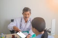 Asian Senior man doctor talking to female patient in doctors office. Royalty Free Stock Photo