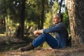 asian senior man with grey hair and beard sitting under a big tree in the forest park in the morning sun Royalty Free Stock Photo