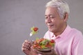 Asian senior man in joyful postures with hand holding salad bowl