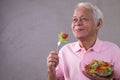 Asian senior man in joyful postures with hand holding salad bowl