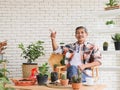 Asian senior man with mustache sitting  at table indoor with houseplants and gardening tool , pointing to copy splace ,smiling , Royalty Free Stock Photo