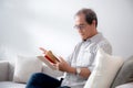 Asian senior man reading a book sitting on sofa with relax in living room at home, elderly man reading literature on couch. Royalty Free Stock Photo