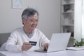 Asian senior man using Laptop and credit card payment shopping online with customer network connection via omni channel system Royalty Free Stock Photo