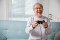 Asian senior old man enjoying holding joystick playing video game at home Royalty Free Stock Photo