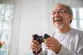 Asian senior old man enjoying holding joystick playing video game at home Royalty Free Stock Photo