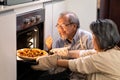 Asian Senior older couple grandparents making pizza in kitchen at home. Aged woman open oven and bring food out from machine. Royalty Free Stock Photo