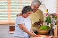 Asian senior wife slicing tomatoes on wooden cutting board and using tablet computer to searching menu recipe.senior with