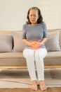 Asian senior woman having stomach pain while sitting on sofa at home, Royalty Free Stock Photo