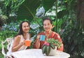 Asian senior woman and her daughter  sitting together at white table in beautiful garden, drinking coffee from blue and orange cup Royalty Free Stock Photo
