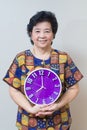 Asian senior woman holding purple clock in studio shot, specialt Royalty Free Stock Photo