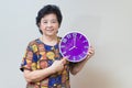 Asian senior woman holding purple clock in studio shot, specialt Royalty Free Stock Photo