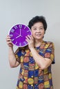 Asian senior woman holding purple clock in studio shot, specialt Royalty Free Stock Photo