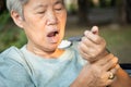 Asian senior woman holding spoon and hands tremor while eating rice,cause of hands shaking include parkinson`s disease,stroke,