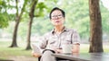 Asian senior woman reading book drinking coffee in sunny park, g